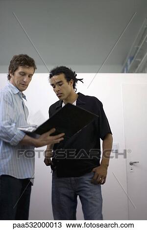 Men standing together looking over contents of binder View Large Photo Image Stock Image - Men standing together looking over contents of binder. Fotosearch