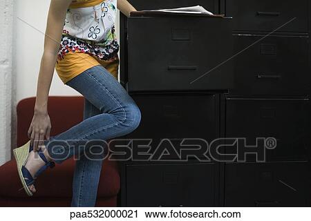 Woman adjusting shoe, leaning against filing cabinet View Large Photo Image Stock Image - Woman adjusting shoe, leaning against filing cabinet. Fotosearch