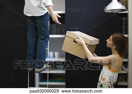 Stock Photo - Woman handing box to man standing on ladder. Fotosearch