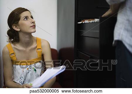 Woman holding document, looking up at colleague using filing cabinet View Large Photo Image Stock Photography - Woman holding document, looking up at colleague using filing cabinet. Fotosearch
