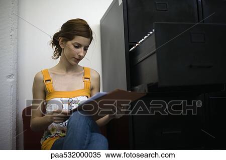 Woman reading document, sitting next to filing cabinet View Large Photo Image Stock Photography - Woman reading document, sitting next to filing cabinet. Fotosearch