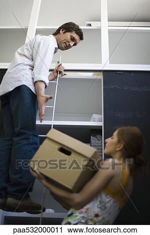 Woman struggling to lift heavy box up to man standing on ladder View Large Photo Image Stock Image - Woman struggling to lift heavy box up to man standing on ladder. Fotosearch