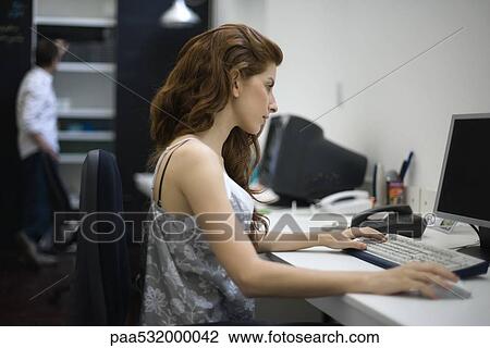 Woman working at desk, colleague standing in background View Large Photo Image Stock Image - Woman working at desk, colleague standing in background. Fotosearch