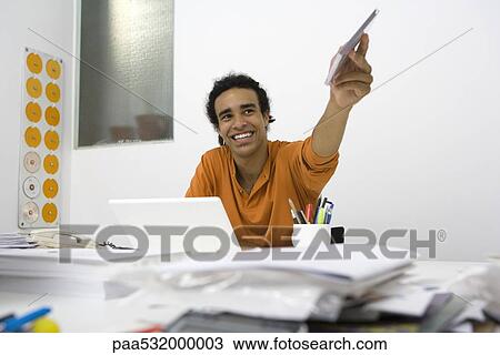 Young man sitting at messy desk, holding out CD case View Large Photo Image Stock Image - Young man sitting at messy desk, holding out CD case. Fotosearch