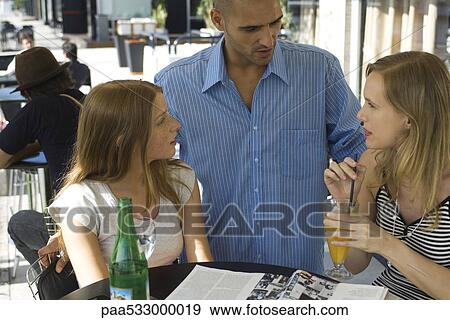 Stock Photo - Man talking to two young women at outdoor cafe. Fotosearch