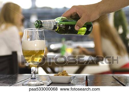 Stock Photo - Pouring beer into glass at sidewalk cafe. Fotosearch