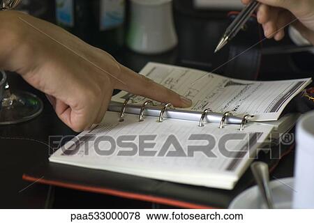 Two people making plans using agenda, one holding pen while the other points to page View Large Photo Image Stock Photo - Two people making plans using agenda, one holding pen while the other points to page. Fotosearch