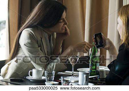 Two women sitting in cafe, looking at photophone together View Large Photo Image Stock Photography - Two women sitting in cafe, looking at photophone together. Fotosearch