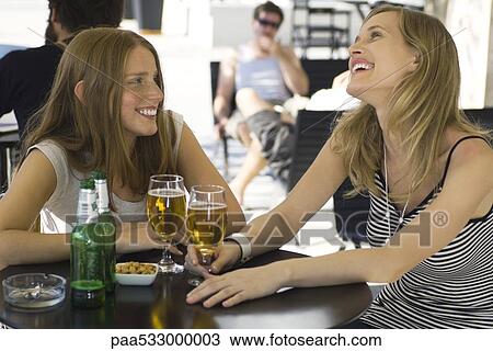 Two young female friends sitting at outdoor cafe with glasses of beer View Large Photo Image Stock Image - Two young female friends sitting at outdoor cafe with glasses of beer. Fotosearch