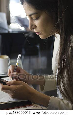 Stock Photograph - Woman copying information from cell phone into agenda. Fotosearch
