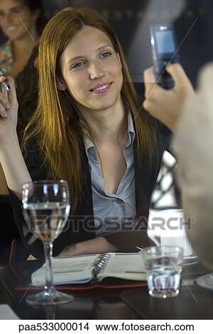 Picture - Woman posing for photo taken with cell phone in cafe. Fotosearch