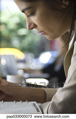 Stock Image - Woman sitting in cafe, looking at agenda, close-up. Fotosearch