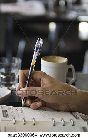 Woman sitting in cafe, writing in agenda, cropped view of hand View Large Photo Image Picture - Woman sitting in cafe, writing in agenda, cropped view of hand. Fotosearch