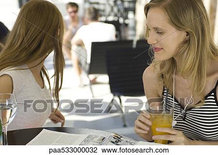 Woman sitting in outdoor cafe with friend, reading magazine View Large Photo Image Stock Image - Woman sitting in outdoor cafe with friend, reading magazine. Fotosearch