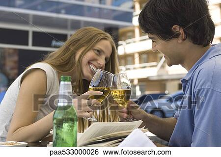 Stock Photograph - Young couple clinking glasses of beer at outdoor cafe. Fotosearch