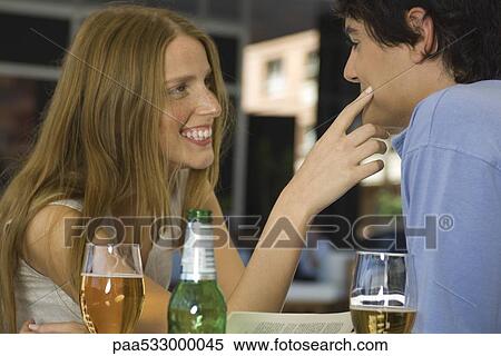 Stock Photography - Young couple in cafe, woman touching man's cheek. Fotosearch