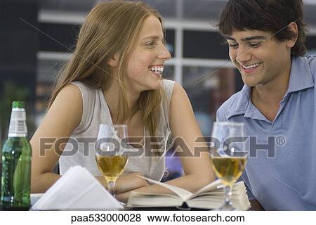 Young couple sitting at outdoor cafe, looking at book together View Large Photo Image Stock Photo - Young couple sitting at outdoor cafe, looking at book together. Fotosearch