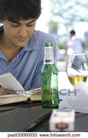 Young man reading book and having a beer at an outdoor cafe View Large Photo Image Stock Image - Young man reading book and having a beer at an outdoor cafe. Fotosearch
