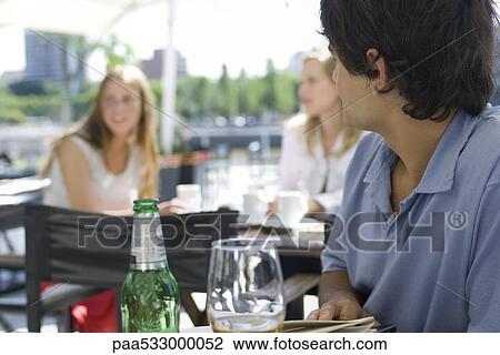 Young man sitting at outside cafe, looking over shoulder at young women sitting behind him View Large Photo Image Stock Image - Young man sitting at outside cafe, looking over shoulder at young women sitting behind him. Fotosearch