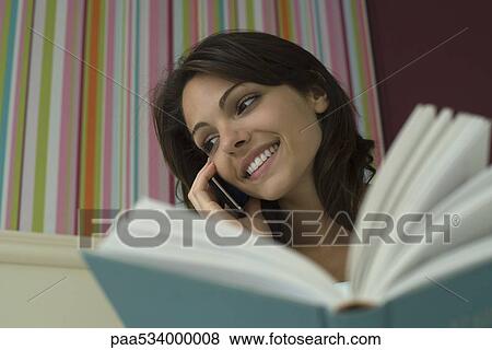Woman holding book and using cell phone, low angle view View Large Photo Image Stock Photo - Woman holding book and using cell phone, low angle view. Fotosearch