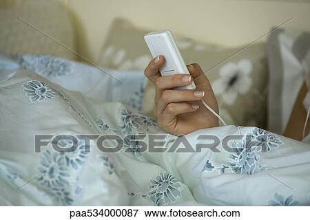 Stock Photo - Woman in bed, holding MP3 player, cropped view of hand. Fotosearch