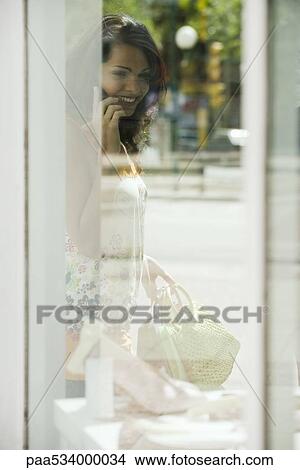 Woman looking in shop window, talking on cell phone View Large Photo Image Picture - Woman looking in shop window, talking on cell phone. Fotosearch