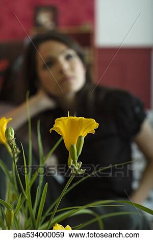 Stock Photo - Woman sitting, holding head, focus on flowering plant in foreground. Fotosearch