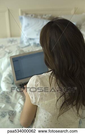 Woman using laptop on bed, rear view View Large Photo Image Stock Image - Woman using laptop on bed, rear view. Fotosearch