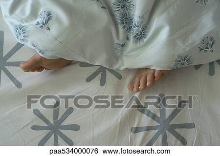 Stock Photograph - Woman's feet sticking out from under duvet. Fotosearch