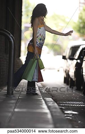 Young woman hailing taxi, carrying shopping bags View Large Photo Image Picture - Young woman hailing taxi, carrying shopping bags. Fotosearch