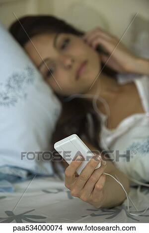 Young woman lying in bed, listening to MP3 player View Large Photo Image Picture - Young woman lying in bed, listening to MP3 player. Fotosearch