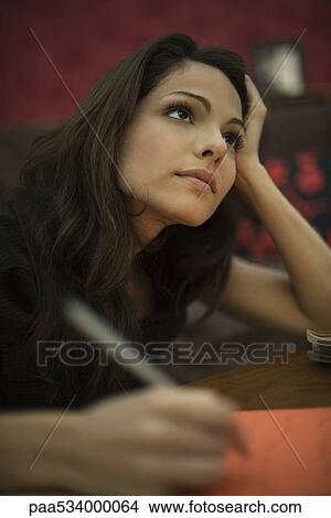 Young woman writing, looking up in thought View Large Photo Image Picture - Young woman writing, looking up in thought. Fotosearch
