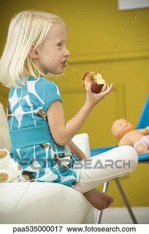 Little girl eating apple on sofa, side view View Large Photo Image Stock Photo - Little girl eating apple on sofa, side view. Fotosearch