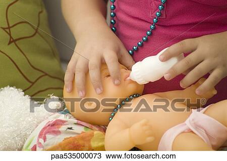 Stock Image - Little girl feeding baby doll with bottle, cropped view. Fotosearch