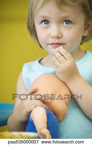 Little girl holding baby doll, eating snack View Large Photo Image Stock Photo - Little girl holding baby doll, eating snack. Fotosearch