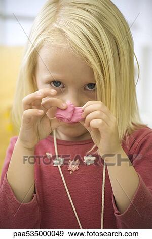 Stock Photo - Little girl holding pink clay in front of face, portrait. Fotosearch