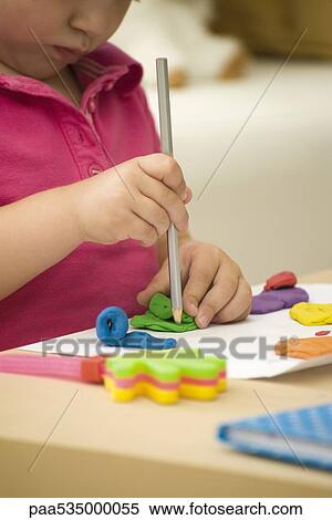 Stock Photography - Little girl shaping colorful clay with pencil, cropped view. Fotosearch