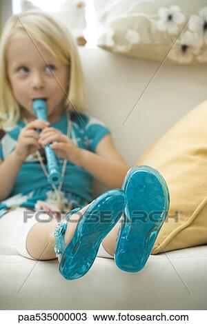 Stock Image - Little girl sitting on sofa, playing recorder. Fotosearch