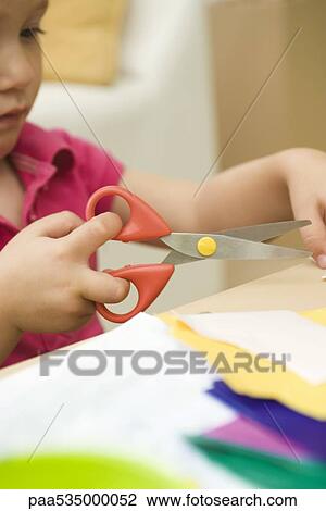 Stock Image - Little girl using scissors to cut paper, cropped view. Fotosearch
