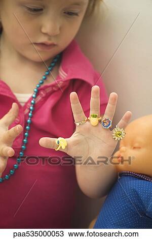 Little girl wearing plastic rings on every finger, looking at hand View Large Photo Image Stock Image - Little girl wearing plastic rings on every finger, looking at hand. Fotosearch