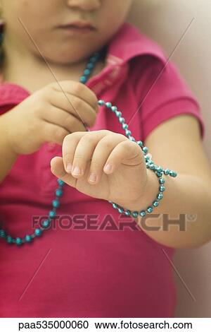 Stock Image - Little girl wrapping beaded necklace around wrist, cropped. Fotosearch