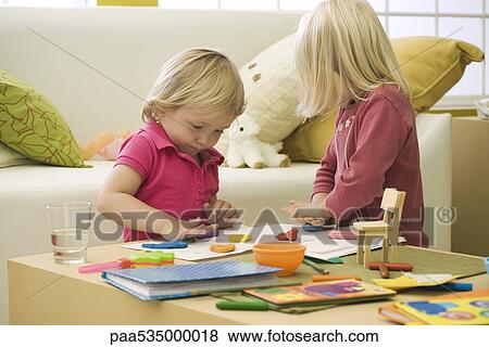 Stock Photo - Little girls playing with clay on coffee table. Fotosearch