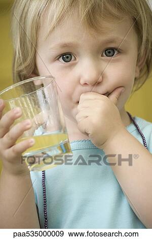 Toddler girl holding glass of juice, covering mouth with one hand View Large Photo Image Stock Photo - Toddler girl holding glass of juice, covering mouth with one hand. Fotosearch