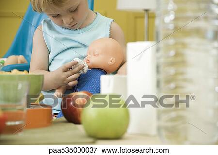 Stock Photo - Toddler girl playing with baby doll at table. Fotosearch