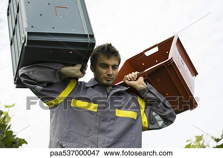 Stock Photo - France, Champagne-Ardenne, Aube, man carrying plastic bins, low angle view. Fotosearch