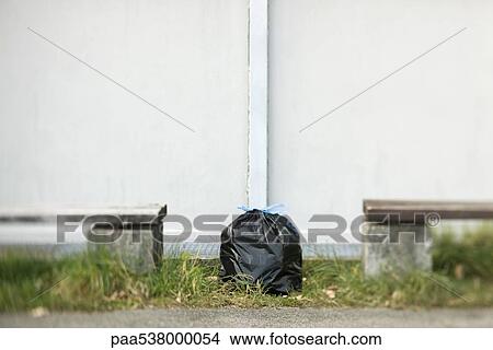Picture - Garbage bag sitting on ground between two benches. Fotosearch