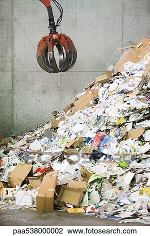 Stock Image - Grapple hanging over heap of paper in recycling center. Fotosearch