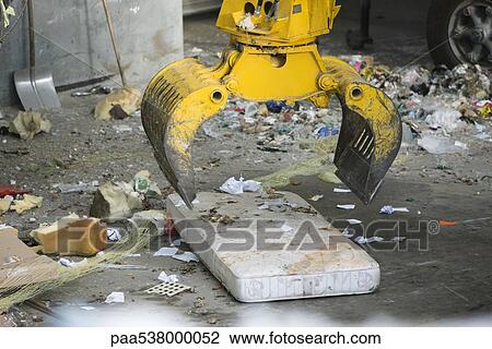 Stock Image - Grapple picking up mattress in garbage dump. Fotosearch