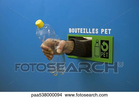 Picture - Hand reaching from inside recycling receptacle, holding plastic bottle. Fotosearch