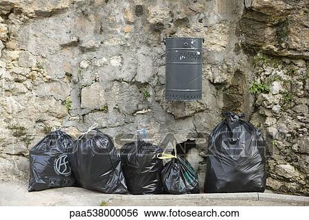 Several bags of garbage lined up along stone wall beneath mounted trash can View Large Photo Image Stock Photograph - Several bags of garbage lined up along stone wall beneath mounted trash can. Fotosearch